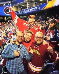 Three supporters in arena seats with a mascot behind them
