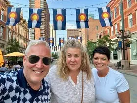 Three people gathered beneath Colorado flags on a city street